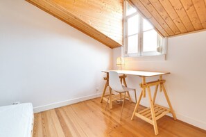 Ein Zimmer mit geneigter Holzdecke, einem weißen Schreibtisch mit Stuhl und einem Fenster.