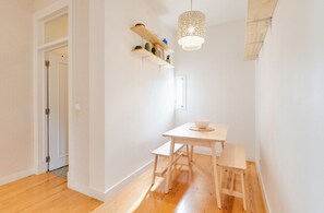 Ein Zimmer mit Holzboden, einem weißen Tisch mit zwei Stühlen, einer Pendelleuchte und einem Holzregal mit Dekorationen.