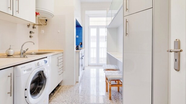 Un pasillo estrecho que da a un balcón con vistas, una lavadora y un lavabo.