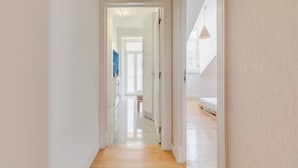 Un pasillo con piso de madera que conduce a una habitación con cama y lámpara colgante.