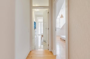 Ein Flur mit Holzboden, der zu einem Zimmer mit einem Bett und einer Pendelleuchte führt.