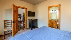 Een slaapkamer met een bed, een houten stoel, een dressoir, een televisie en een spiegel in de badkamer.