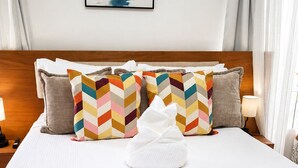 A neatly made bed with a white comforter and a white towel, two colorful chevron-patterned pillows, and a wooden headboard. - Luxury 2BR Penthouse /Rooftop Jacuzzi/ Pool/Near Beach (Punta Cana)