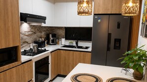 A modern kitchen with wooden cabinets, a stainless steel refrigerator, a gas stove, and two hanging pendant lights. - Luxury 2BR Penthouse /Rooftop Jacuzzi/ Pool/Near Beach (Punta Cana)