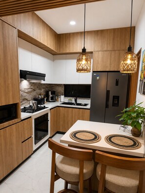 Eine moderne Küche mit Holzschränken, einem Edelstahlkühlschrank, einem Gasherd und zwei Pendelleuchten.