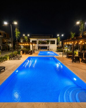 Ein Schwimmbecken mit Holzterrasse, Liegestühlen und Lichterketten.