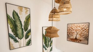 A staircase with wooden steps and a handrail, a wall with three framed botanical prints, and a hanging woven light fixture. - Luxury 2BR Penthouse /Rooftop Jacuzzi/ Pool/Near Beach (Punta Cana)