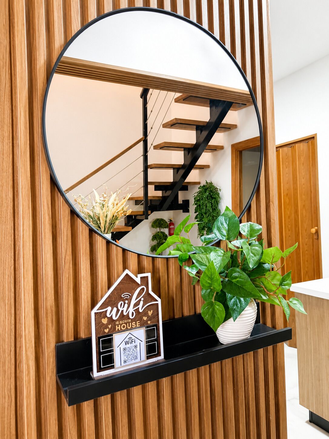 Ein Spiegel spiegelt eine Treppe und einen Blumentopf an einer Holzwand wider.