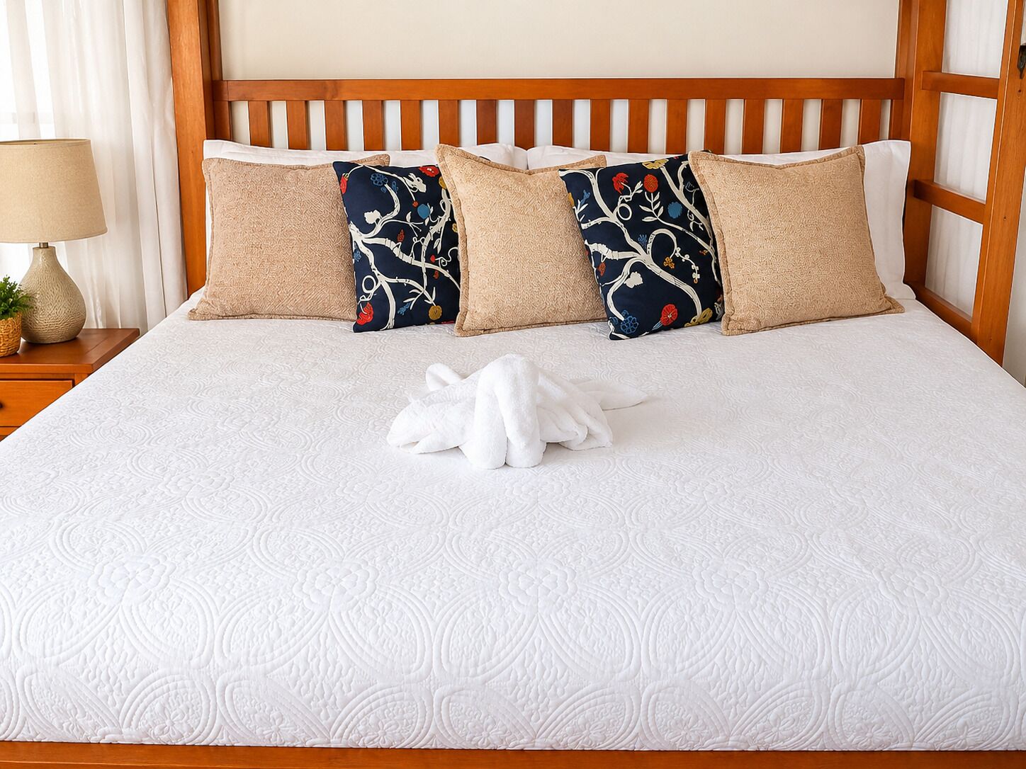 A neatly made bed with a white quilt, two patterned pillows, and a white towel.