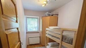 Ein kleines Zimmer mit Etagenbett, Heizkörper, Fenster mit Jalousien und Tür.