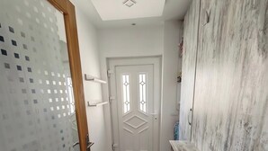 Ein Flur mit einer Holztür, einer weißen Tür mit einem geometrischen Fenster und einem Schrank mit strukturierter Oberfläche.
