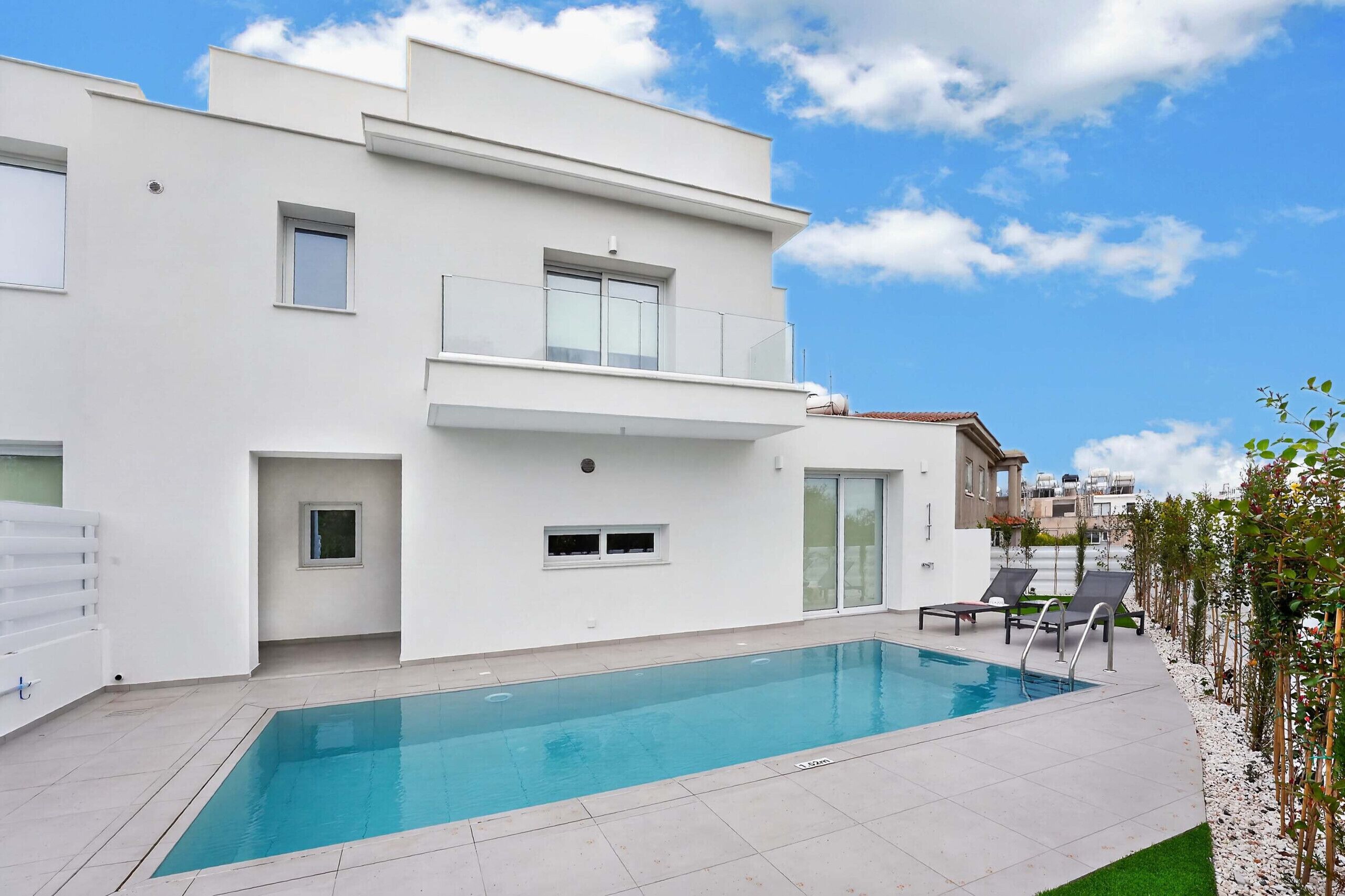 A modern two-story building with a swimming pool, a balcony, and a view of the sky.