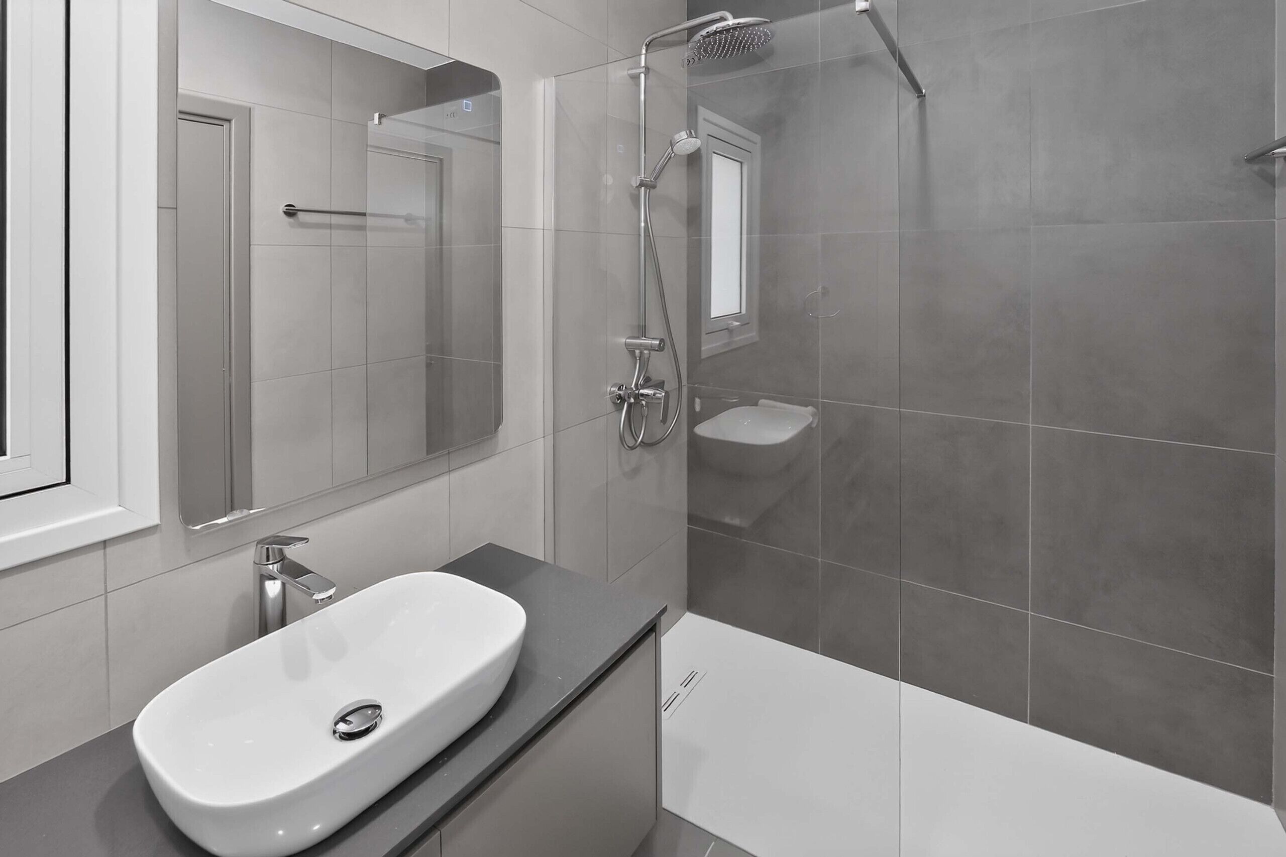 A modern bathroom with a white sink, a glass shower enclosure, and a large mirror.