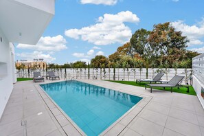 A rectangular swimming pool with a tiled deck, surrounded by lounge chairs and a white fence. - Eclipse: New Private 4-Bed Villa, Central Napa (Ayia Napa)