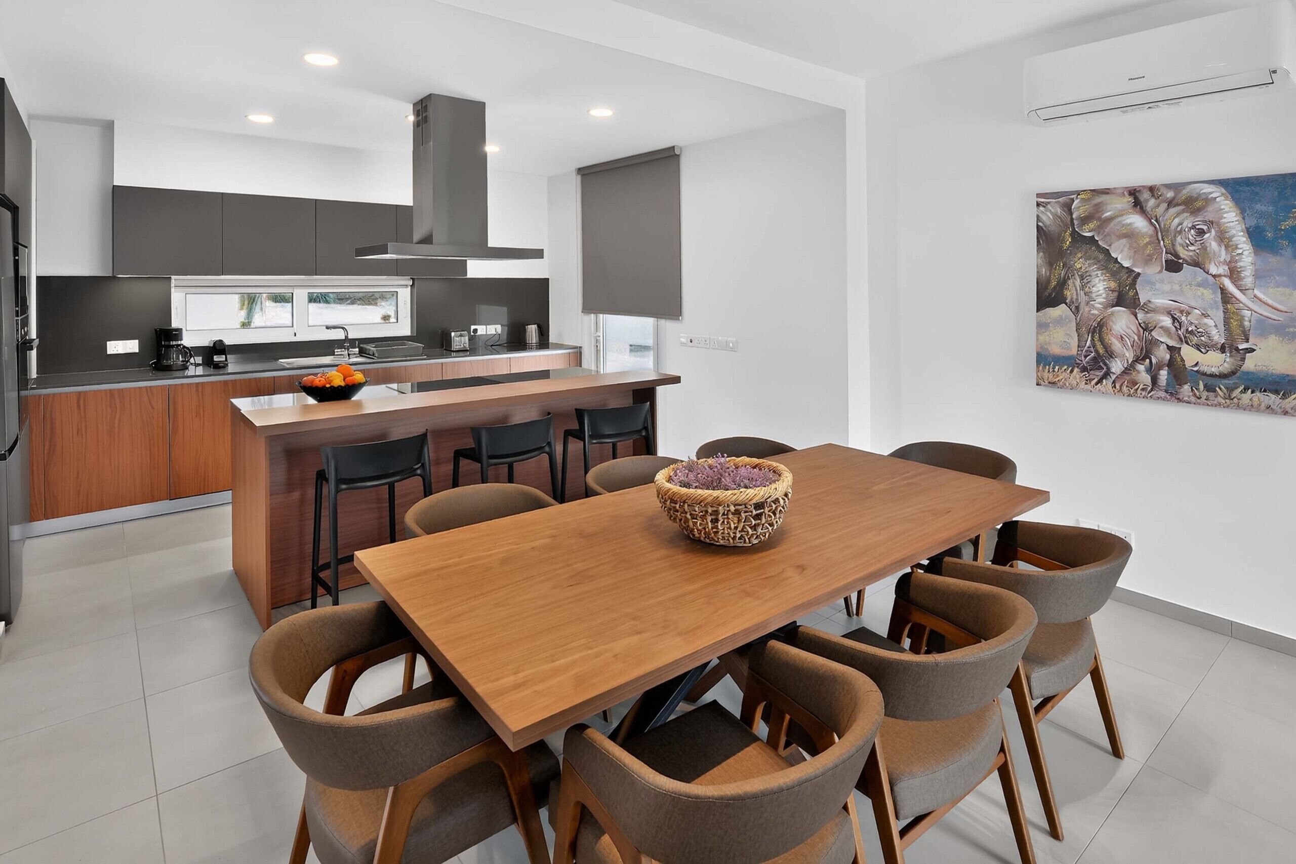 A modern kitchen with a central island, a dining area with a wooden table and chairs, and a large painting on the wall.