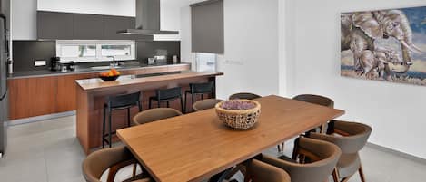 Una cocina moderna con una isla central, un comedor con mesa y sillas de madera, y un cuadro grande en la pared.