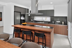 A modern kitchen with a central island, bar stools, and a dining table. - Eclipse: New Private 4-Bed Villa, Central Napa (Ayia Napa)