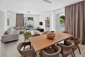 A modern living room with a sofa, coffee table, and dining area with chairs. - Celeste: Private 4BDR Villa, Central Napa (Ayia Napa)