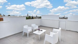 En tagterrasse med hvide stole og et bord, en klar blå himmel og udsigt over bybilledet.