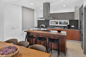 A modern kitchen with a central island, bar stools, and a dining table with a basket of flowers. - Celeste: Private 4BDR Villa, Central Napa (Ayia Napa)