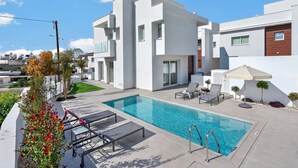 En moderne boligbygning med swimmingpool, udendørs siddepladser og en velplejet have.