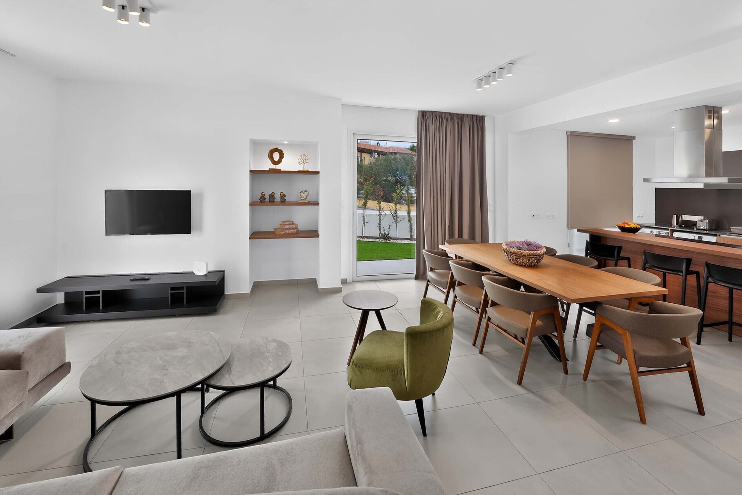 A modern living room with a flat-screen TV, a sofa, a coffee table, and a dining area with a wooden table and chairs.