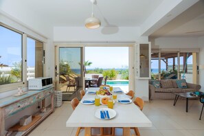 A modern kitchen with a dining area, a pool view, and a sofa with a view. - Artisan Seafront Villa - Escape (Protaras)