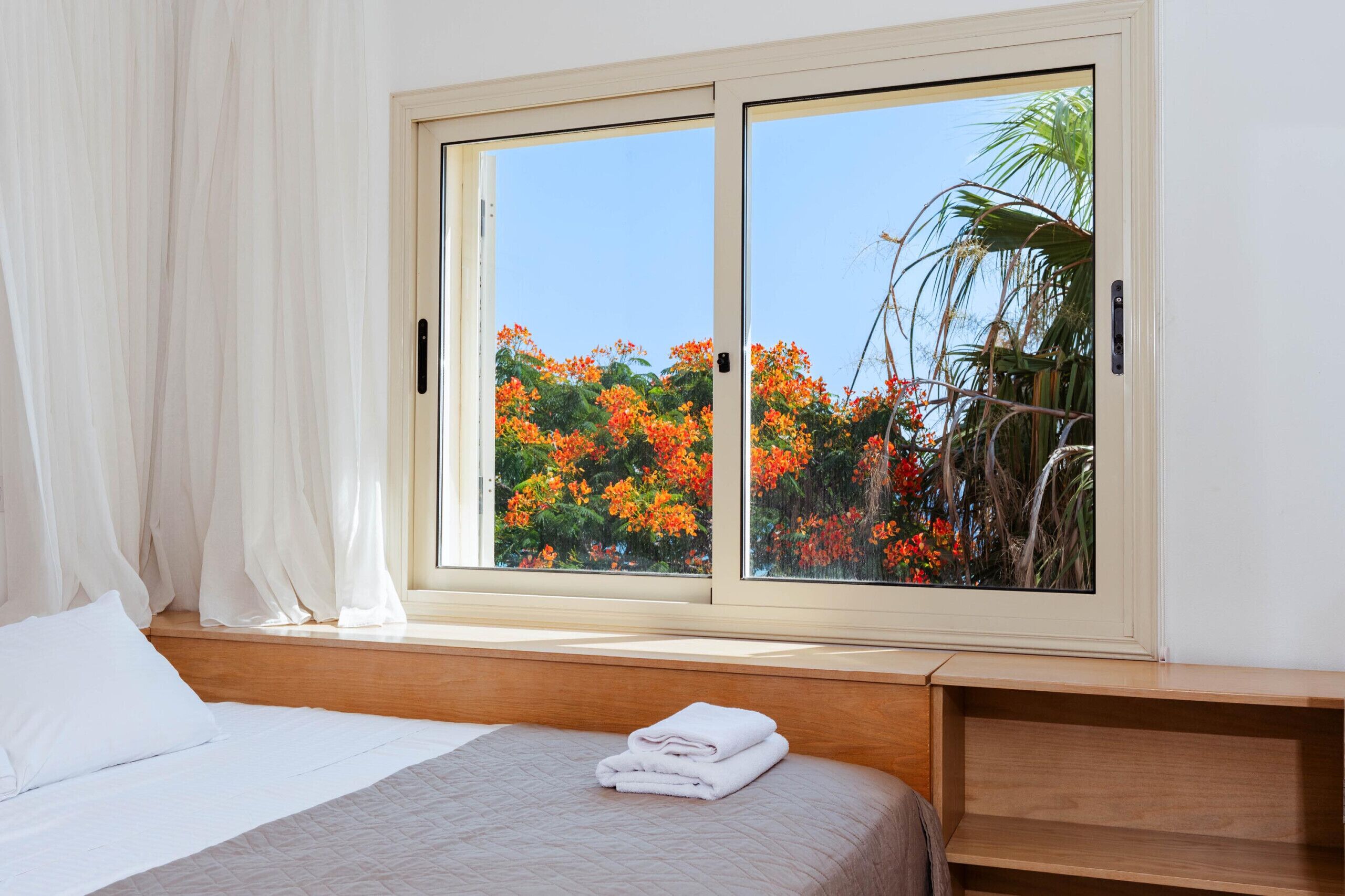 A bedroom with a large window, a bed, a wooden headboard, and a nightstand.