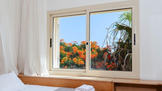 A bedroom with a large window, a bed, a wooden headboard, and a nightstand. - Artisan Seafront Villa - Treehouse (Protaras)