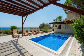 A swimming pool with lounge chairs, a pergola, and a view of the sea. - Artisan Seafront Villa - Treehouse (Protaras)