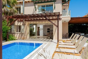 A poolside area with lounge chairs, a pergola, and a view of the house's interior. - Artisan Seafront Villa - Treehouse (Protaras)