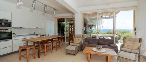 A modern kitchen with a dining area, wicker furniture, and a view through large glass doors.