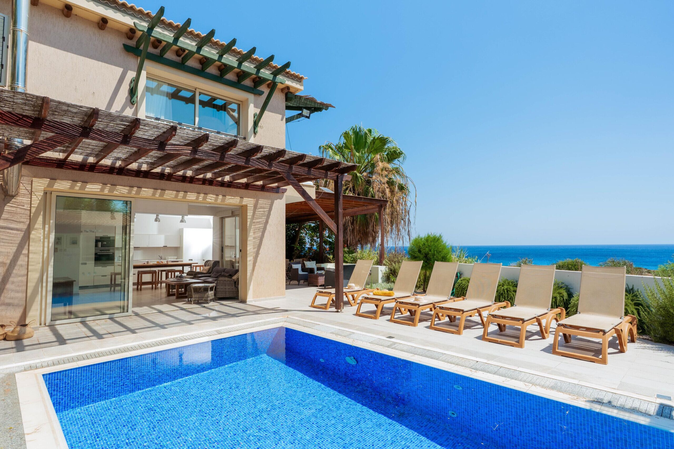 Un espace aménagé au bord de la piscine offrant une vue dégagée sur l’océan, un coin salon extérieur abrité et un bâtiment moderne doté de grandes fenêtres.