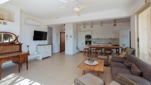 A spacious living area with a sofa, a coffee table, a television, and a ceiling fan. - Artisan Seafront Villa - Treehouse (Protaras)