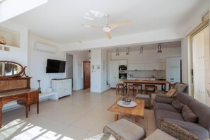 A spacious living area with a sofa, a coffee table, a television, and a ceiling fan. - Artisan Seafront Villa - Treehouse (Protaras)