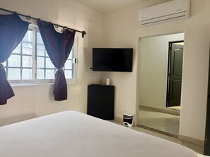 Ein Schlafzimmer mit Bett, Fernseher, Kleiderschrank und einem Fenster mit Vorhängen.
