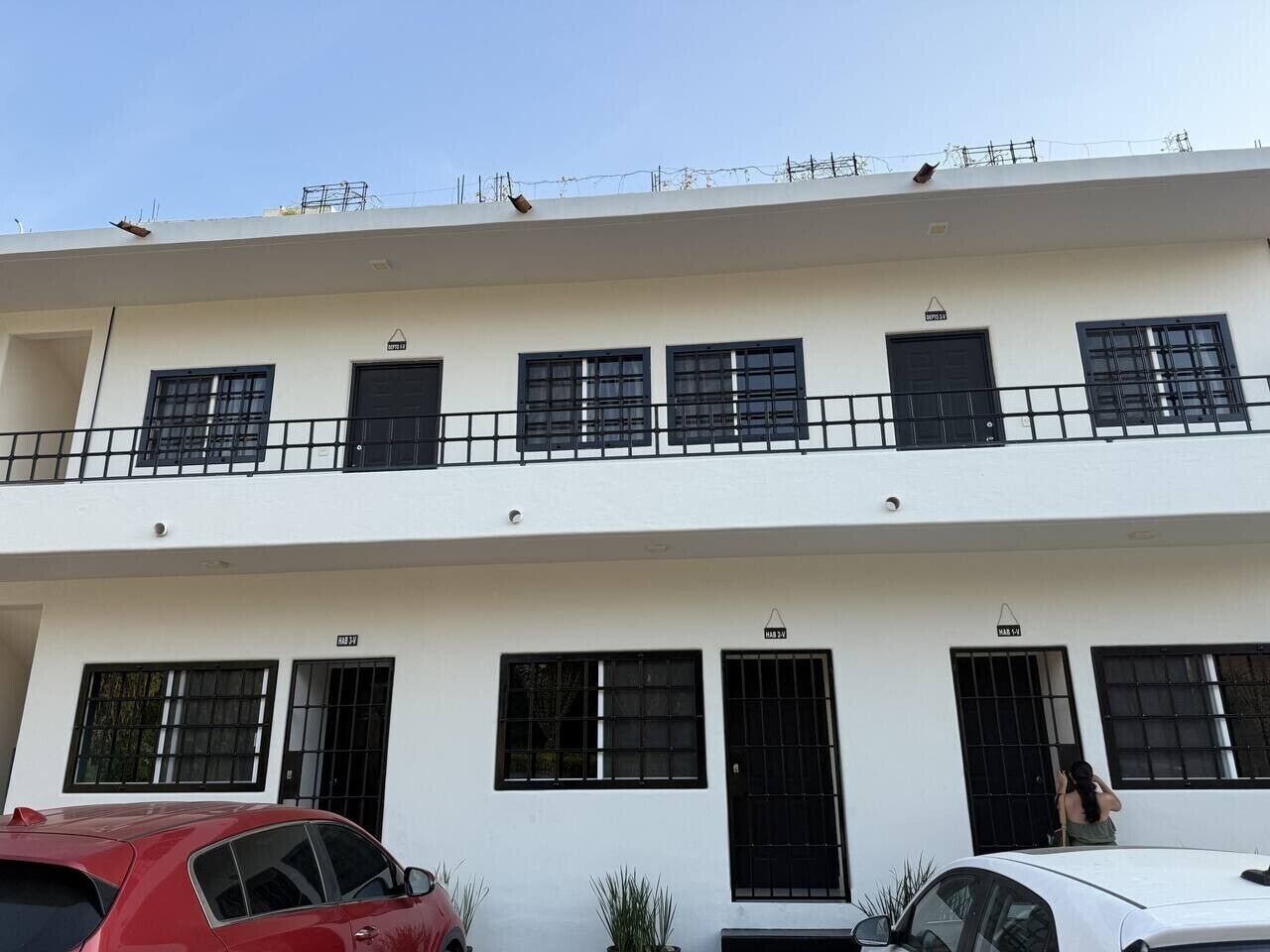 Un bâtiment à deux étages, doté de nombreuses fenêtres et portes, dont certaines sont munies de barreaux en métal. Des voitures sont garées devant.