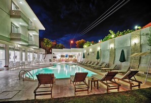 Zona de piscina con sillones de descanso y un edificio con balcón.
