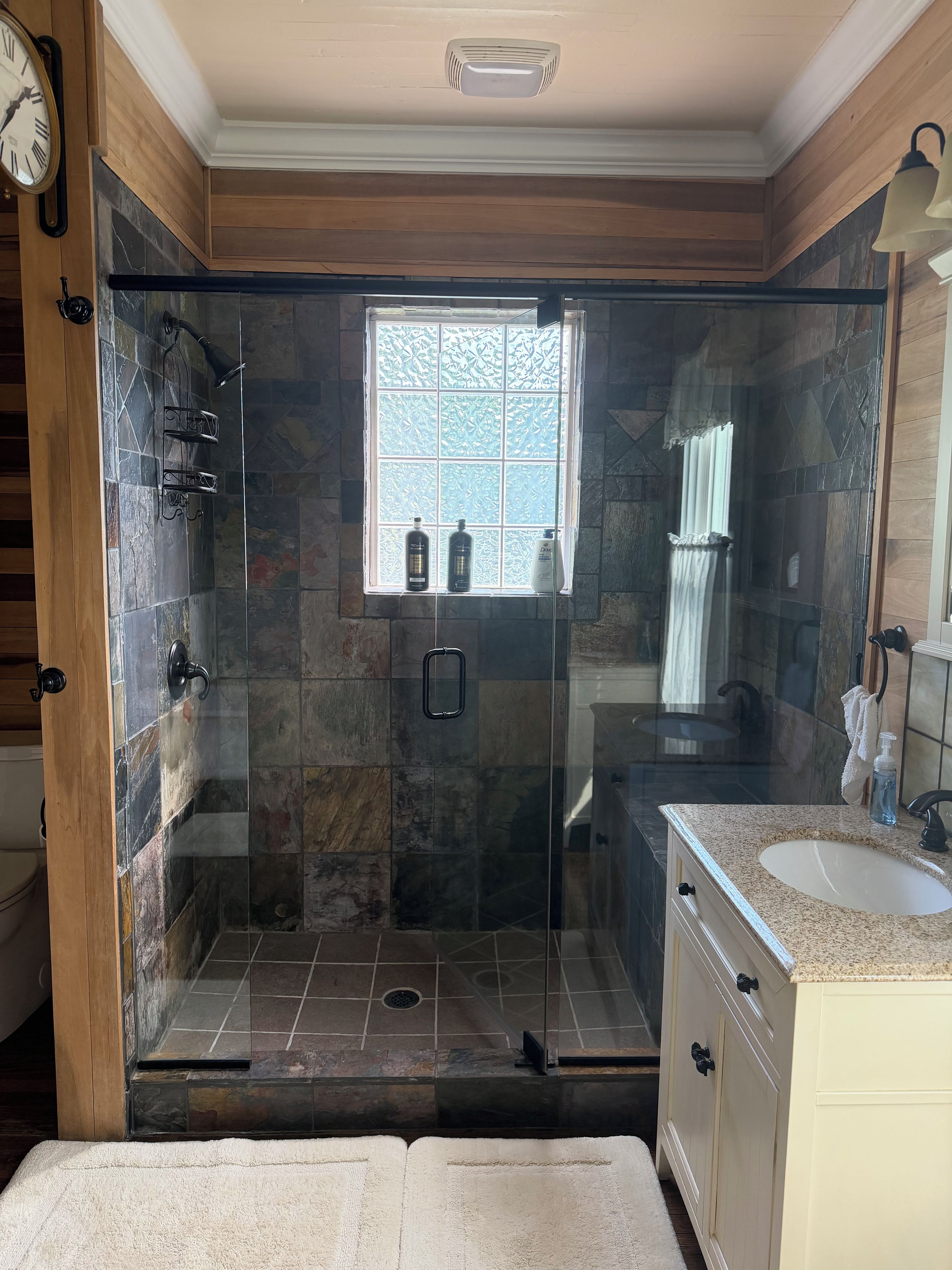Une salle de bain avec une douche à parois de verre, une fenêtre et un meuble-lavabo avec un évier.