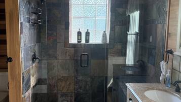 Une salle de bain avec une douche à parois de verre, une fenêtre et un meuble-lavabo avec un évier.