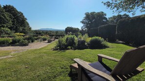 Um jardim com um banco de madeira, um caminho de cascalho e sebes bem aparadas.