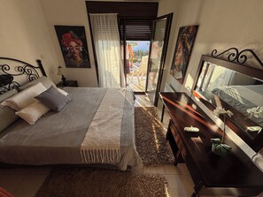 Quarto com cama, mesa de cabeceira, cômoda e janela com vista.