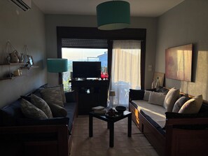 A living room with a sofa, a coffee table, a TV, and a view through a window. - Halkidikigr (Nikiti)