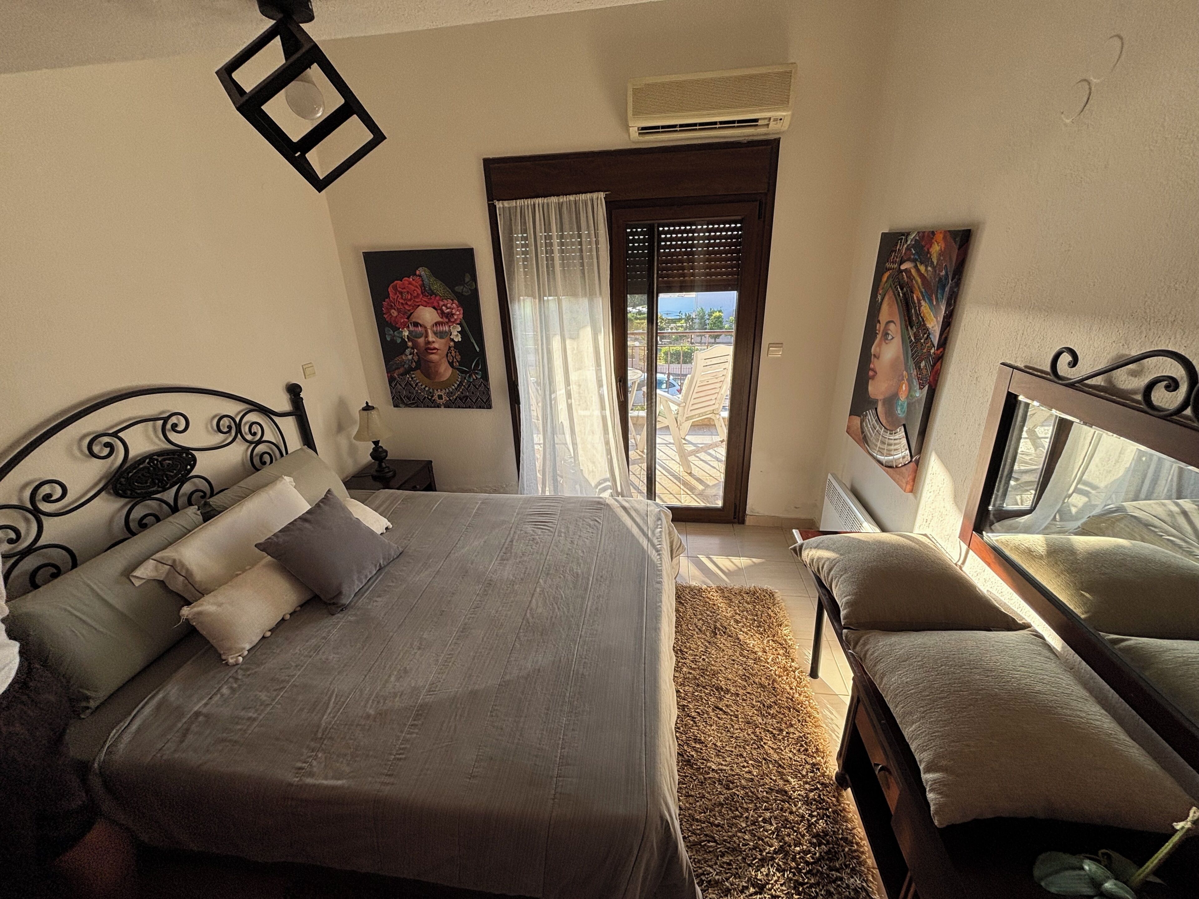 A bedroom with a bed, a nightstand, a window with curtains, and a painting on the wall.