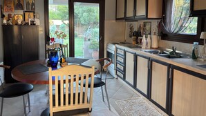 A modern kitchen with a dining area, featuring a wooden table, chairs, and a view of the garden through the sliding glass door. - Halkidikigr (Nikiti)