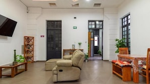 A spacious lobby with a sofa, wooden table, and chairs, a TV mounted on the wall, and a door with an emergency exit sign. - Hostel Bemaro Mexico City (Mexico City)