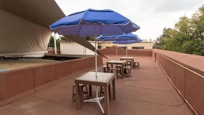 An outdoor patio area with tables and blue umbrellas, surrounded by a low wall. - Hostel Bemaro Mexico City (Mexico City)