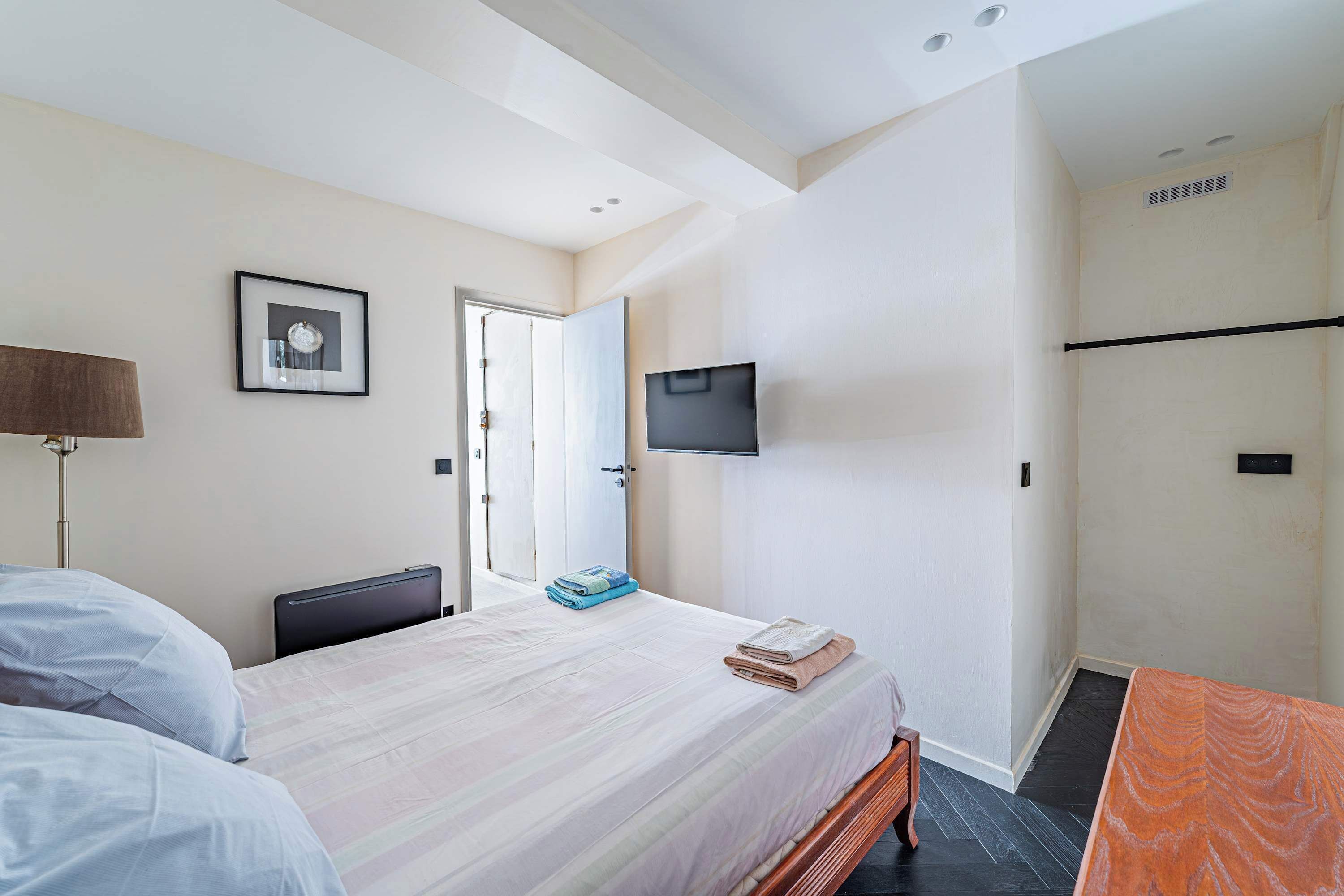 A hotel room with a bed, a desk, a TV mounted on the wall, and a door leading to another room.