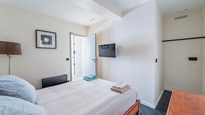Una habitación de hotel con cama, escritorio, televisor montado en la pared y puerta que da a otra habitación.