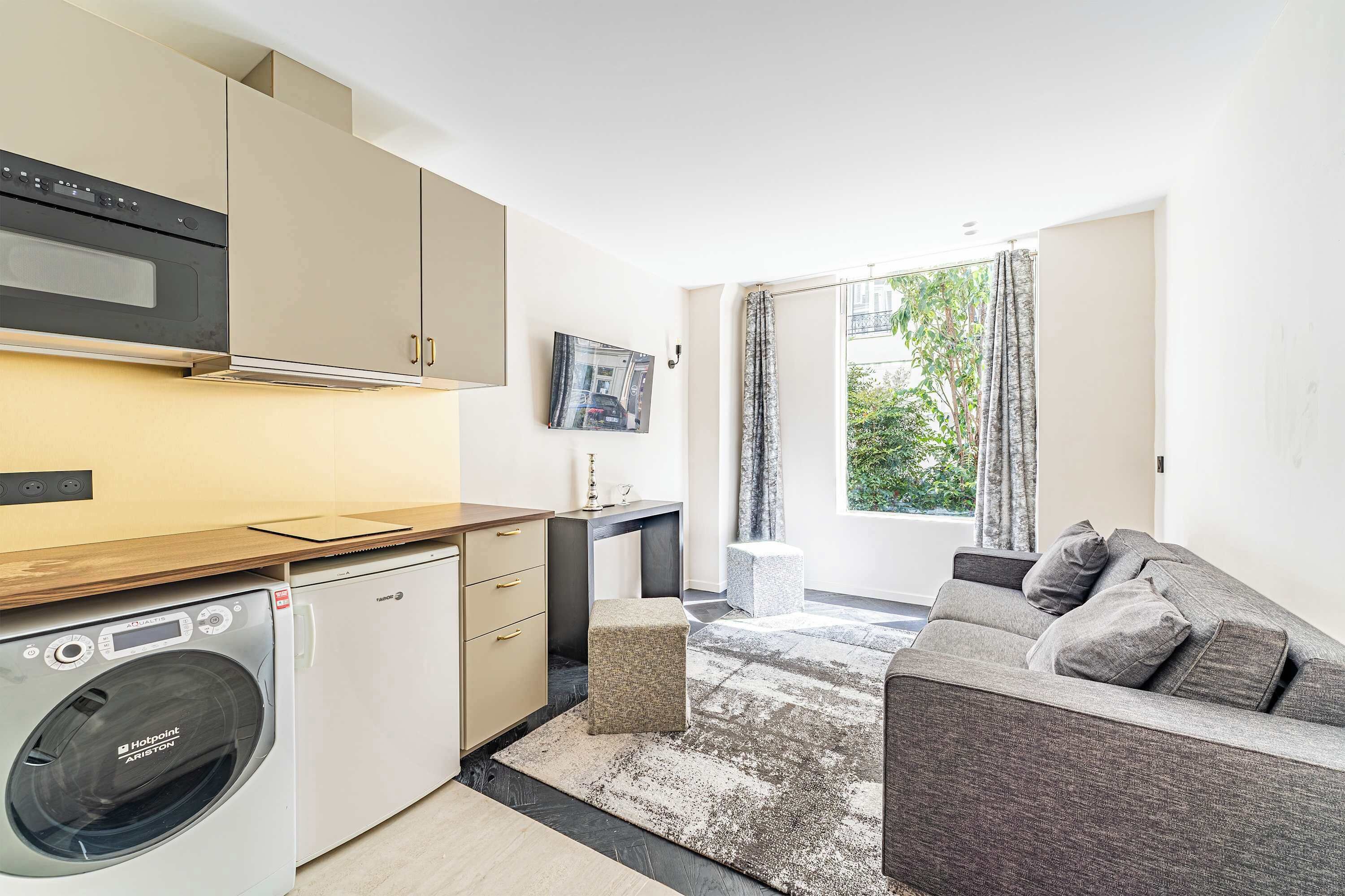 A compact kitchen with modern appliances, a sofa, and a view of the outdoors.